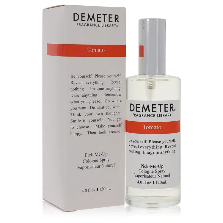 Clear glass rectangular bottle of Demeter Tomato cologne spray placed on rich, dark potting soil surrounded by fresh, green tomato leaves with realistic dew drops.
